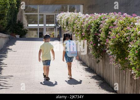 Un jeune enfant qui retourne à l'école. Une petite fille avec un sac à dos de teinture de cravate marche à l'école avec son frère. Banque D'Images