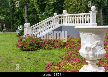 escaliers blancs dans le parc avec de l'herbe verte et des fleurs rouges près d'un vase blanc Banque D'Images