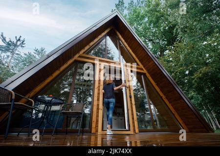 Vue arrière d'une femme ouvrant la porte d'un chalet forestier et entrant à l'intérieur Banque D'Images