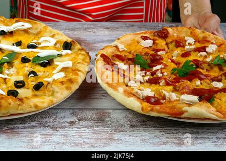 Le chef met sur table deux pizzas faites maison avec du fromage, des saucisses, de la viande de poulet, des olives et des feuilles de basilic. Délicieux en-cas malsain de restauration rapide de la Méditerranée FO Banque D'Images