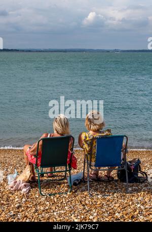 deux femmes plus âgées assises sur une plage dans des chaises en conversation, deux femmes à la retraite assis ensemble à bavarder au bord de la mer dans des chaises de plage, en prenant facile. Banque D'Images