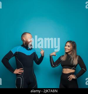 Des amis adorables dans des vêtements de sport souriant tout en se tenant ensemble sur fond bleu Banque D'Images