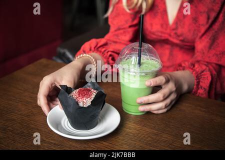 Latte au matcha glacé et gros gâteau dans un café entre les mains des femmes. Banque D'Images