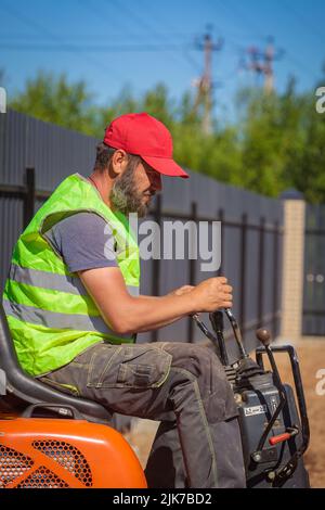 Un homme sur une mini-pelle permet de nivrir un morceau de terre et de détacher le sol Banque D'Images