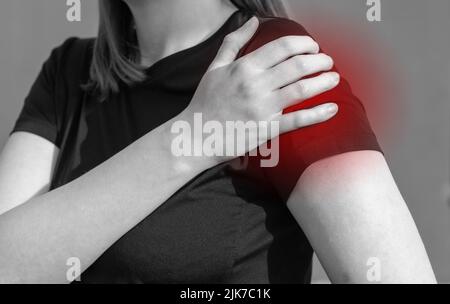 Femme touchant l'épaule douloureuse avec le point rouge. Douleur au bras, enflure. Utilisation excessive, lésions des tendons de la coiffe des rotateurs, conséquences de la luxation. Concept des problèmes de santé. Noir et blanc. Photo de haute qualité Banque D'Images
