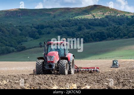 Un agriculteur équipé d'un tracteur McCormick prépare le lit de semence, tandis qu'un tracteur équipé d'un semoir suit. North Yorkshire, Royaume-Uni. Banque D'Images