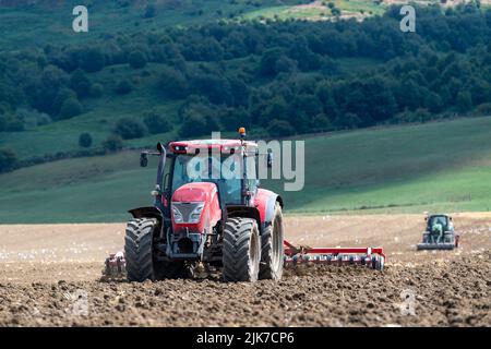 Un agriculteur équipé d'un tracteur McCormick prépare le lit de semence, tandis qu'un tracteur équipé d'un semoir suit. North Yorkshire, Royaume-Uni. Banque D'Images