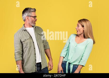 Choqué femme d'âge moyen et son mari regardant l'un l'autre avec des bouches ouvertes, se sentant surpris sur fond jaune Banque D'Images