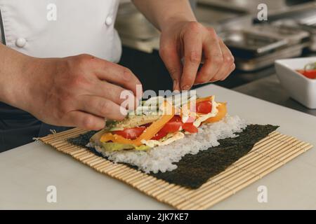 Gros plan des mains du chef préparant des sushis avec tapis de bambou dans la cuisine du restaurant Banque D'Images