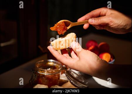 Nourriture et boissons, concept de récolte d'automne d'été. Vue rognée des mains d'une femme au foyer qui étale la confiture d'abricot sur le pain Banque D'Images