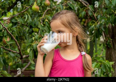 Belle petite fille boit du lait. Arbre avec poires en arrière-plan Banque D'Images