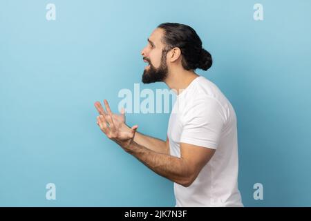 Que voulez-vous ? Vue latérale d'un homme en colère confus debout avec des mains levées et surpris d'expression indignée, demandant pourquoi, quelle raison. Studio d'intérieur isolé sur fond bleu. Banque D'Images