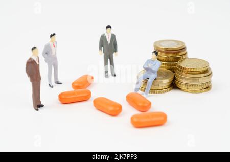 Une figurine miniature d'un homme est assise sur des pièces de monnaie, à côté de lui sont des pilules et des figurines de personnes. Concept d'entreprise médicale Banque D'Images