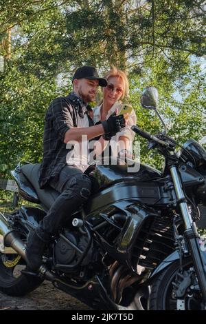 Couple d'âge moyen utilisant un téléphone portable, assis sur une moto, voyageant ensemble sur une route forestière Banque D'Images