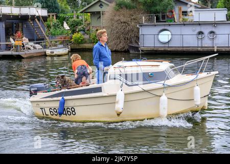 Petits moteurs de bateau de croisière en cabine blanche le long de la Tamise avec un homme qui dirige le bateau et une femme et un chien à l'arrière. Péniche dans backgroung Banque D'Images