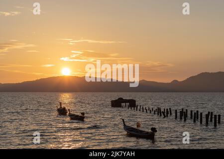 Coucher de soleil sur l'île tropicale. Un vieux quai cassé dans la mer avec des bateaux de pêche à longue queue amarré et le soleil se coucher sur les collines d'une île tropicale Banque D'Images