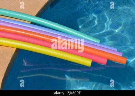 Des vibes d'été. Nouilles de bain aux couleurs arc-en-ciel flottant sur le côté de la piscine Banque D'Images