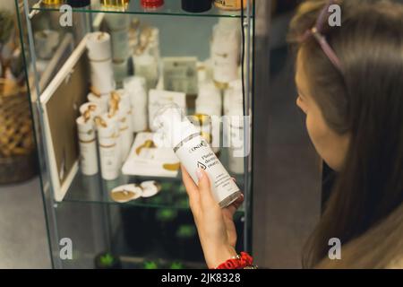 05.28.2022 Varsovie, Pologne. Femme caucasienne à cheveux longs tenant un produit médical lié aux mauvaises herbes dans une main et lisant sur ses avantages. Vitrine en verre avec d'autres produits CBG CBD en arrière-plan. Photo de haute qualité Banque D'Images