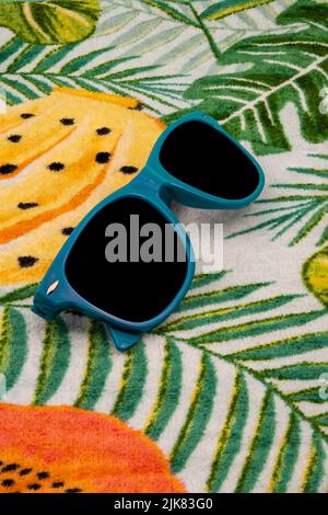Lunettes de soleil bleues sur une serviette hawaïenne. Banque D'Images