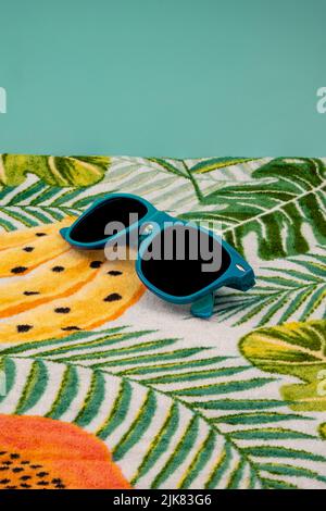 Lunettes de soleil bleues sur une serviette hawaïenne. Banque D'Images