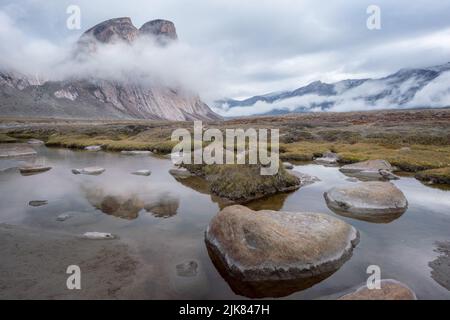 Les majestueuses roches de granit se reflètent dans la surface de l'eau. Paysage arctique sauvage du col d'Akshayuk, île de Baffin, Canada un jour pluvieux et nuageux d'été arctique Banque D'Images