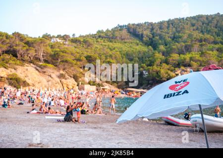 Ibiza, espagne - 25 juillet 2022: Parapluie de plage avec nous aimons texte Ibiza sur une plage avec des vacanciers défocused en arrière-plan. Banque D'Images