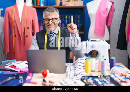 Hispanique tailleur homme avec cheveux gris faisant appel vidéo souriant avec une idée ou une question pointant du doigt avec le visage heureux, numéro un Banque D'Images