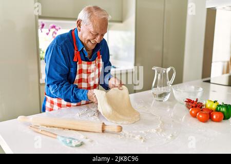 Homme âgé souriant confiant tenant la pâte avec les mains dans la cuisine Banque D'Images