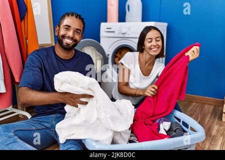 Homme et femme couple souriant confiant laver les vêtements à la blanchisserie Banque D'Images