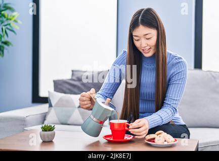 Femme chinoise qui verse du café sur une tasse, assise sur un canapé à la maison Banque D'Images