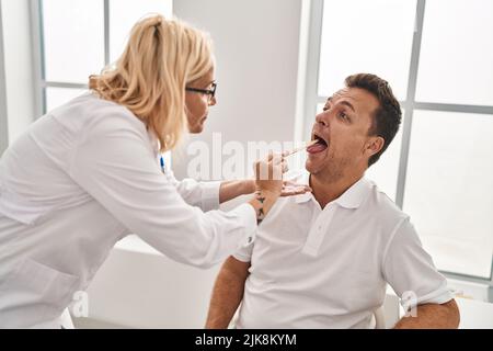 Homme et femme d'âge moyen médecin et patient examinant la gorge ayant une consultation médicale à la clinique Banque D'Images