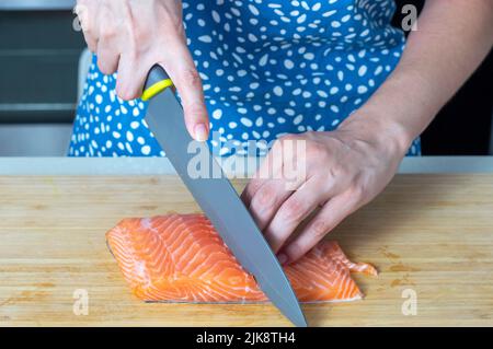 Femme coupant du filet de saumon frais sur une planche en bois Banque D'Images