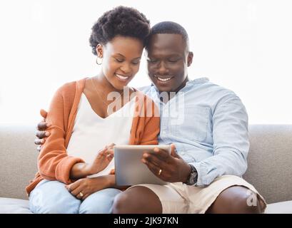 Ce sont les petites choses qui créent les plus grands souvenirs : un jeune couple assis sur le canapé tout en utilisant une tablette numérique à la maison. Banque D'Images