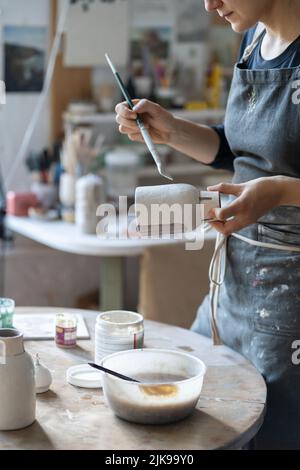 Jeune artisan peint vase avec pinceau après la cuisson et façonnage fait à la main en studio Banque D'Images