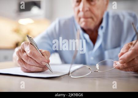 Admin ne sait pas d'âge. Un homme âgé remplissant des formes à la table de cuisine à la maison. Banque D'Images