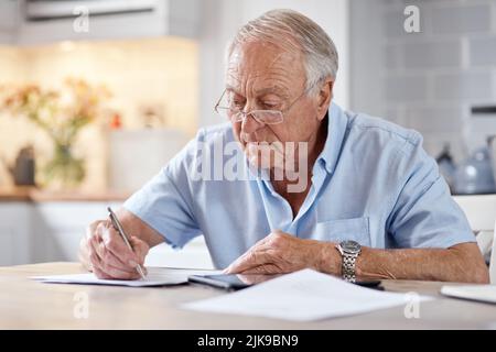 Il semble qu'il soit écrit, mais on ne peut pas lire entre les lignes. Un homme âgé remplissant des formes à la table de cuisine à la maison. Banque D'Images