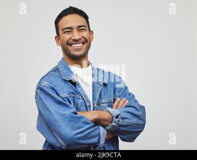 Bonheur et confiance. Portrait court d'un beau jeune homme debout avec ses bras pliés en studio sur fond gris. Banque D'Images