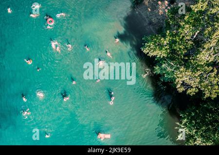 Vue de dessus de drone aérienne vers le bas de personnes méconnaissables nageant dans le lac. Belle eau bleue avec beaucoup de gens se reposent sur la plage, nager et sauter dans l'étang ou la rivière. Heure d'été au lac, tir de drone Banque D'Images