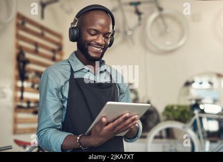 J'ai un travail si détendu. Un beau jeune homme debout seul dans son magasin de vélos et utilisant une tablette numérique tout en portant des écouteurs. Banque D'Images