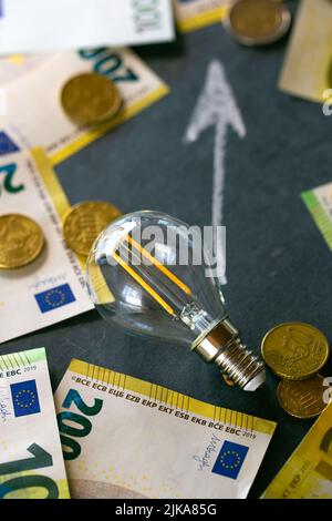 Économiser l'électricité concept.coût de l'électricité.hausse des prix de l'électricité en Europe.ampoule, billets en euros et pièces en euros, en hausse sur une craie noire Banque D'Images