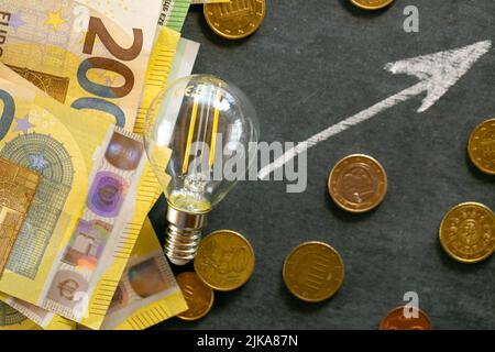 Hausse des prix de l'électricité en Europe. Ampoule, billets en euros et pièces en euros, en hausse sur un tableau noir de craie.crise de la production d'énergie dans l'UE Banque D'Images