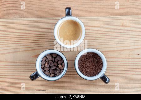 Trois tasses de café. Un avec des grains de café, un avec des grains de café moulus, un avec du café avec du lait sur une table en bois Banque D'Images
