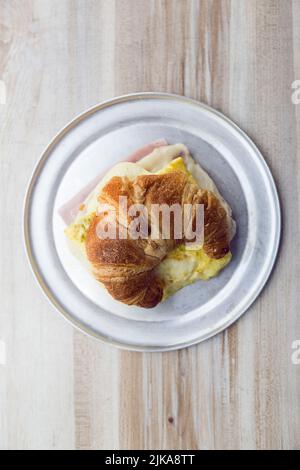 Croissant rempli de jambon et de fromage sur une plaque argentée sur une table en bois Banque D'Images