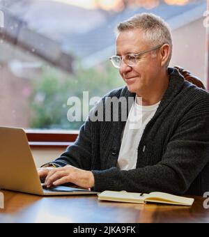 Il travaille sur son plan de retraite. Un beau homme senior travaillant sur son ordinateur portable dans l'étude. Banque D'Images