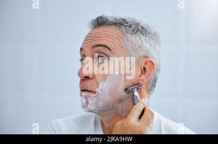C'est l'heure de la barbe. Un homme mûr se rasant le visage dans une salle de bain à la maison. Banque D'Images