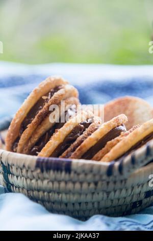 Délicieux biscuits à la noix de coco remplis de caramel dans un panier en osier lors d'un pique-nique sur une nappe bleue Banque D'Images