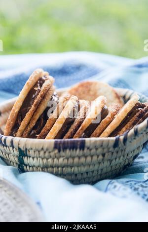 Délicieux biscuits à la noix de coco remplis de caramel dans un panier en osier lors d'un pique-nique sur une nappe bleue Banque D'Images