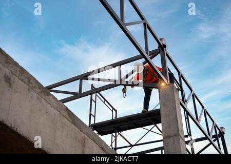 A soudeurs sur les zones à risque. Les soudeurs de treillis de toit en acier travaillent sur la structure de toit avec des dispositifs de sécurité pour empêcher la sécurité de chute au niveau du siège de construction Banque D'Images