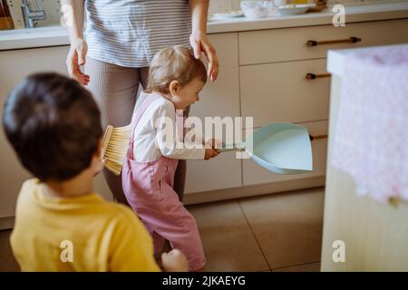 Un petit garçon et une petite fille qui aident à nettoyer la maison à l'aide d'une casserole et d'une brosse qui balaient la saleté du sol. Banque D'Images