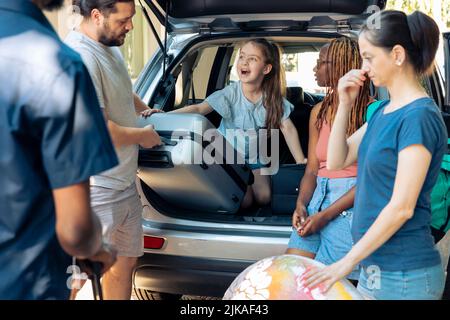 Petit enfant voyageant en vacances en famille, se préparant à aller en vacances au bord de la mer pendant l'été. Des personnes et des amis variés chargent la valise et le chariot dans le coffre de voiture, laissant sur le voyage. Banque D'Images